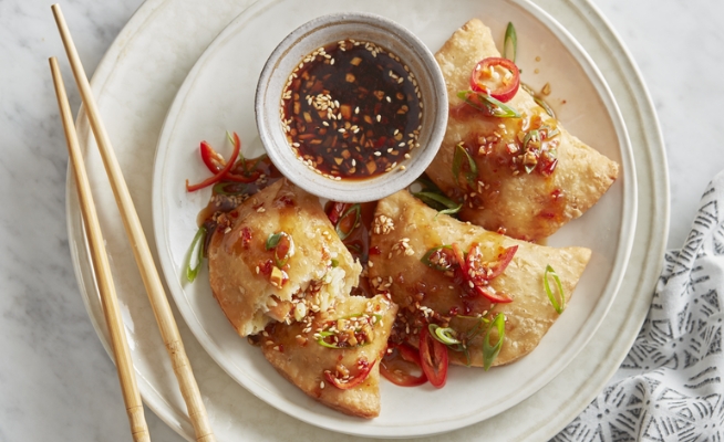 Sweet and Spicy Pork Belly Fried Potstickers with side cup of glaze on top of two stacked white dishes with chopsticks.