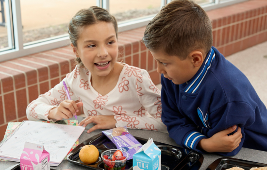 Two students talking at the lunch table while doing homework